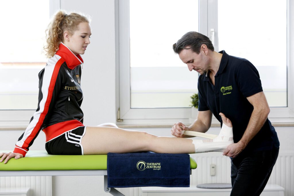 Ein Physiotherapeut bandagiert das Bein einer Sportlerin Therapiezentrums Dormagen.