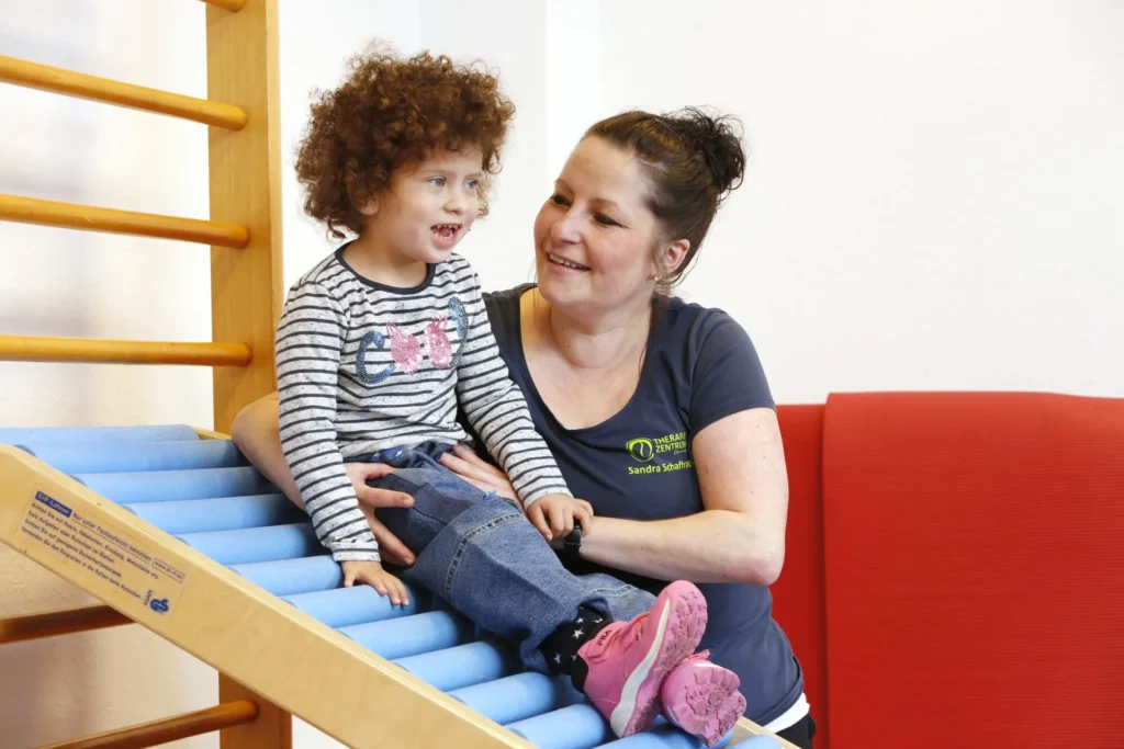 Therapiezentrums Dormagen ist eine Frau, Sie betreut ein Kind auf einem blauen Therapiegerät.
